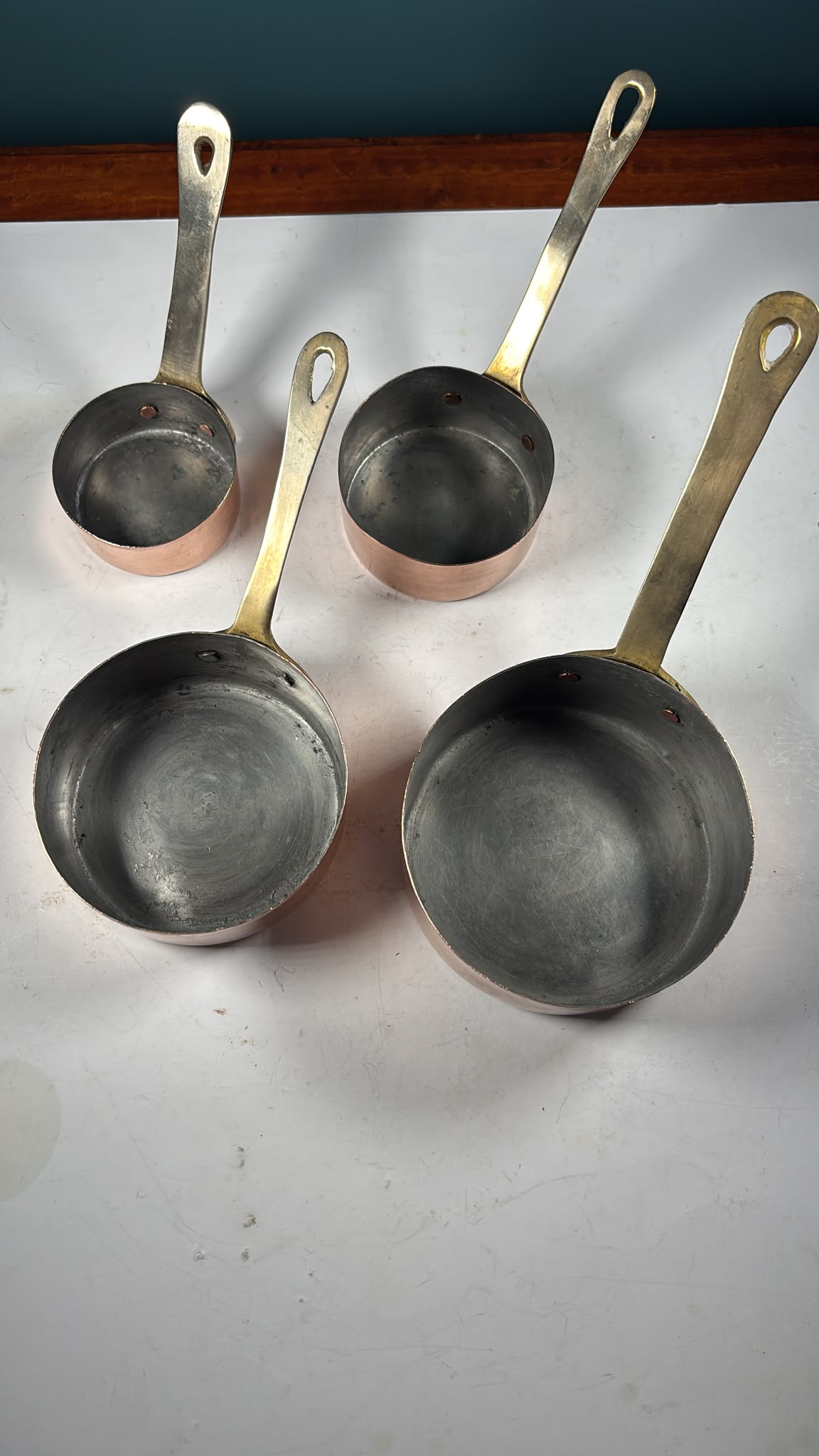 An image of A set of 4 graduated copper mini saucepans with brass handles