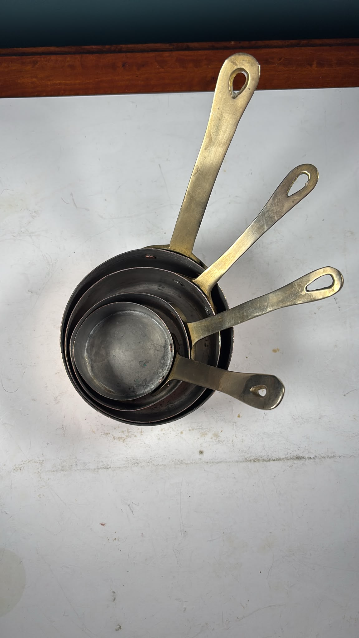 AN image of A set of 4 graduated copper mini saucepans with brass handles